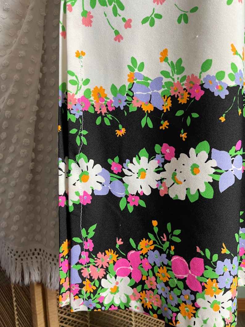 Puede incluir: Una tela negra y blanca con un patr&oacute;n floral. Las flores son rosas, naranjas, verdes y moradas. La tela tiene una costura blanca en el lateral.