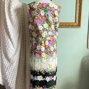 Puede incluir: Un vestido sin mangas con estampado floral en tonos rosa, morado, naranja y verde sobre fondo negro. El vestido tiene un corpi&ntilde;o ajustado y una falda ligeramente acampanada.
