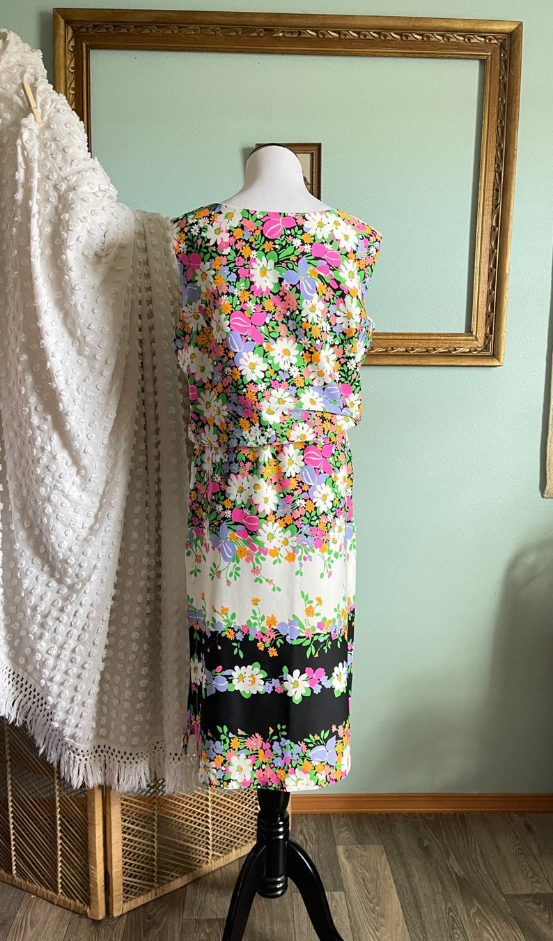Puede incluir: Un vestido sin mangas con estampado floral en tonos rosa, morado, naranja y verde sobre fondo negro. El vestido tiene un corpi&ntilde;o ajustado y una falda ligeramente acampanada.