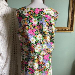 Puede incluir: Un vestido sin mangas con fondo negro y estampado floral colorido. El vestido tiene un corpi&ntilde;o ajustado y una falda fluida.