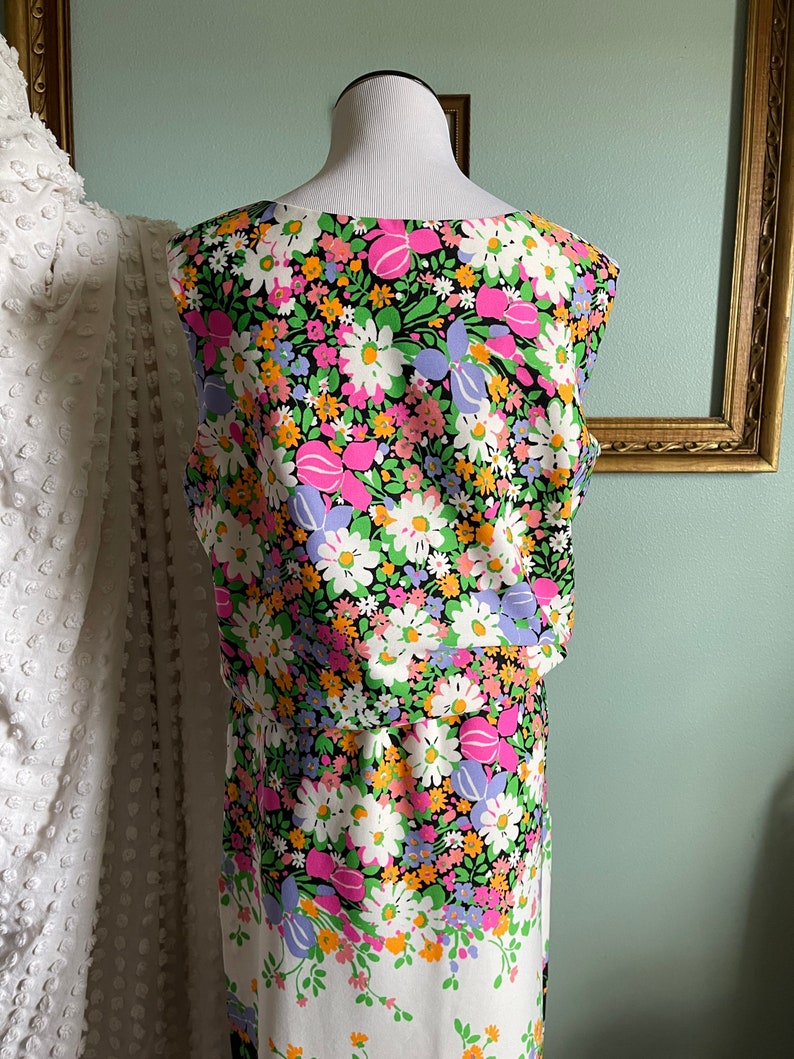 Puede incluir: Un vestido sin mangas con fondo negro y estampado floral colorido. El vestido tiene un corpi&ntilde;o ajustado y una falda fluida.