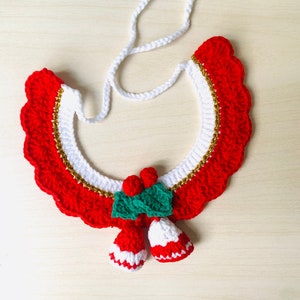 May include: A festive, handmade crochet collar in red and white, adorned with gold trim and two white bell-shaped ornaments. The collar features a scalloped edge and is connected to two white cloud-shaped accents.