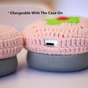 Pu&ograve; includere: Una custodia in crochet rosa per un altoparlante wireless con una porta di ricarica visibile sul lato. Il testo "* Chargeable With The Case On" &egrave; visibile sopra l'altoparlante.