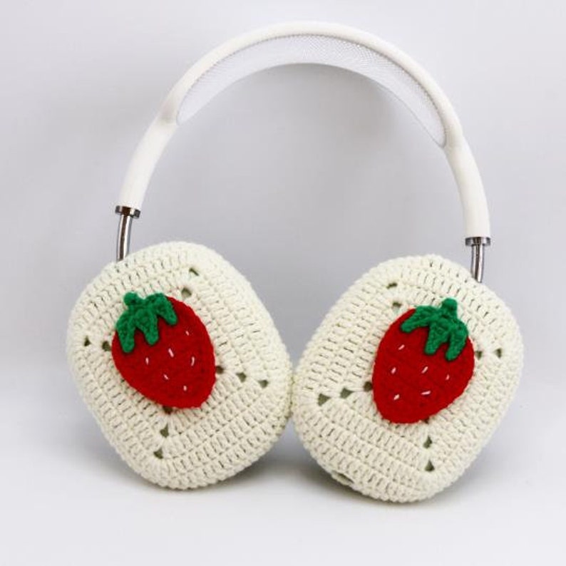 Pode incluir: Capas de fone de ouvido de croch&ecirc; branco com aplica&ccedil;&otilde;es de morango vermelho e verde.