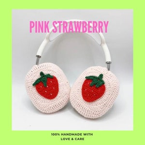 Pode incluir: Protetores de ouvido de croch&ecirc; rosa com um design de morango. Os protetores de ouvido est&atilde;o presos a uma faixa de cabe&ccedil;a branca. "PINK STRAWBERRY" e "100% HANDMADE WITH LOVE & CARE" est&atilde;o escritos na imagem.