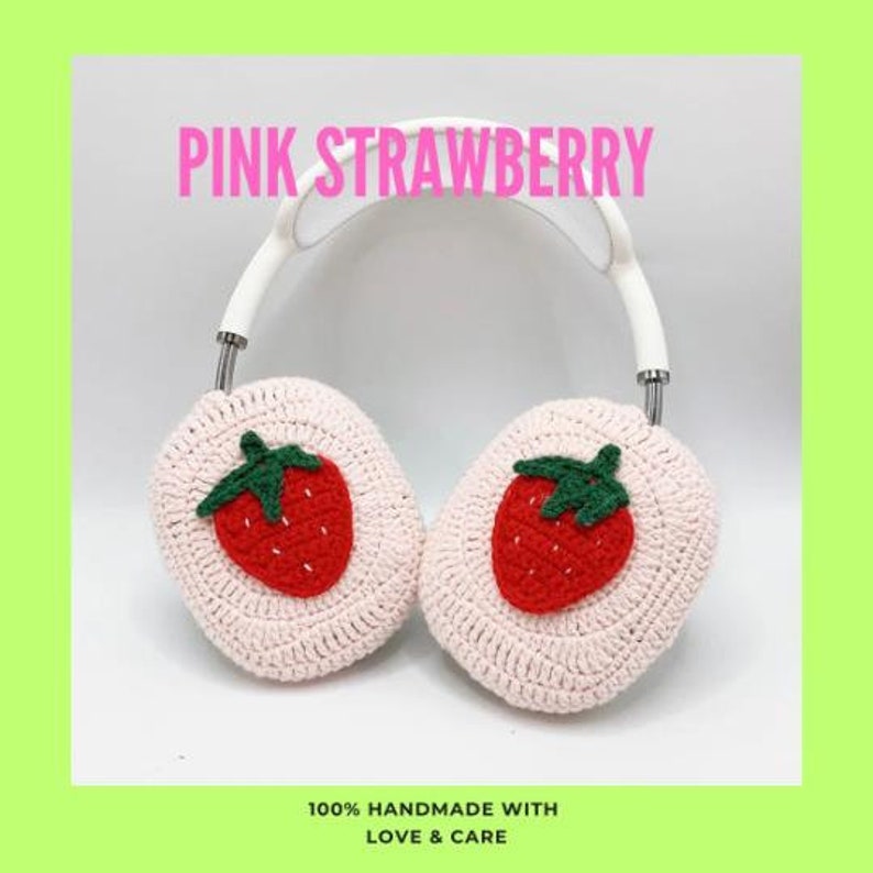 Pode incluir: Protetores de ouvido de croch&ecirc; rosa com um design de morango. Os protetores de ouvido est&atilde;o presos a uma faixa de cabe&ccedil;a branca. "PINK STRAWBERRY" e "100% HANDMADE WITH LOVE & CARE" est&atilde;o escritos na imagem.
