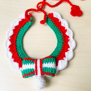May include: A crocheted pet collar in red, white, and green. The collar features a scalloped edge, a bow, and a small bell. The red tie is adjustable. The collar is designed for a pet.