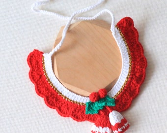 May include: A red, white, and gold crocheted pet collar with a festive design. The collar features a scalloped edge, a white center, and gold trim. A small bell and holly accent the collar, perfect for the holidays.