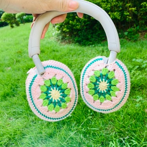 May include: A pair of crocheted earmuffs in pink and green with a white headband. The earmuffs are made with a granny square pattern.
