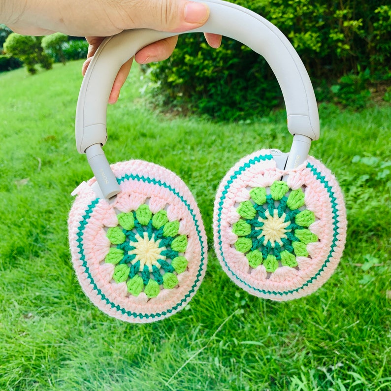 May include: A pair of crocheted earmuffs in pink and green with a white headband. The earmuffs are made with a granny square pattern.