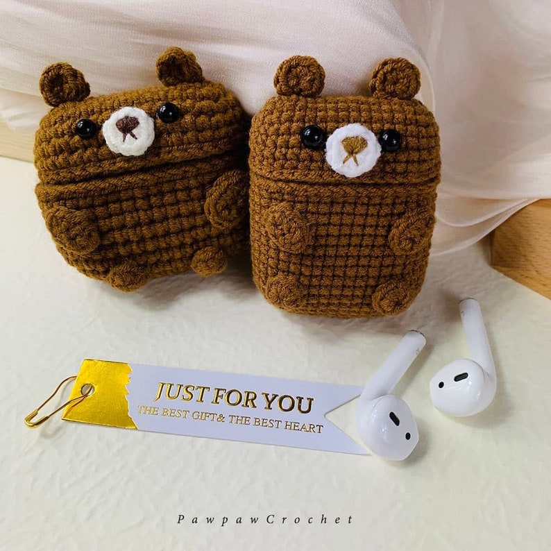 Puede incluir: Dos estuches para Airpods de color marr&oacute;n hechos a crochet con forma de oso, con ojos negros y narices blancas. Los estuches est&aacute;n sobre una superficie blanca con una etiqueta blanca que dice "Just for you, the best gift & the best heart" y una etiqueta dorada con el texto "Pawpaw Crochet".
