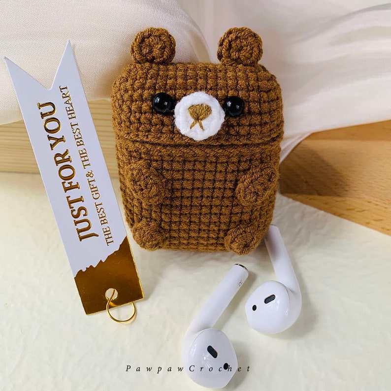 Puede incluir: Una funda de color marr&oacute;n hecha a crochet con forma de oso para auriculares inal&aacute;mbricos. La funda tiene una nariz blanca y ojos negros. El texto "JUST FOR YOU THE BEST GIFT & THE BEST HEART" est&aacute; en una etiqueta blanca con letras doradas.