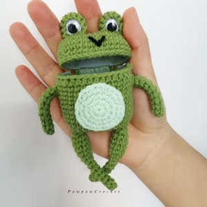 K&ouml;nnte beinhalten: Eine handgefertigte gr&uuml;ne H&auml;kelfrosch mit gro&szlig;en Wackelaugen und einem hellgr&uuml;nen Bauch. Der Mund des Frosches ist offen, und er hat kleine Arme und Beine. Der Text "Pawpaw Crochet" ist unten sichtbar.