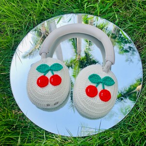 May include: White crocheted headphone covers with red cherries and green leaves. The covers are on a pair of headphones reflected in a mirror.