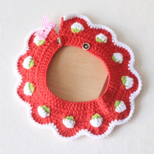 May include: A handmade red crochet bib with white scalloped edges and white and green floral accents. The bib features a pink and white checkered bow and two wooden buttons for closure. A charming accessory for babies.