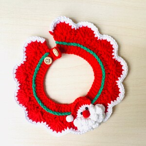 May include: A handmade, crocheted Christmas wreath in red with a white scalloped edge. A green cord accents the wreath's center, and a Santa Claus face is attached. Two wooden buttons secure the wreath.