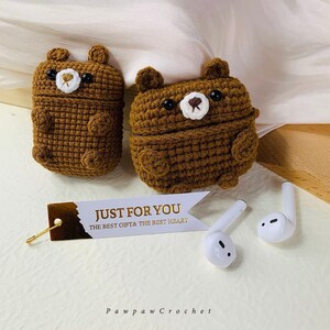Puede incluir: Dos estuches para AirPod de color marr&oacute;n hechos a crochet con forma de oso, con ojos negros y narices blancas. Los estuches est&aacute;n sobre una superficie blanca con una etiqueta dorada que dice "Just for you, the best gift & the best heart".