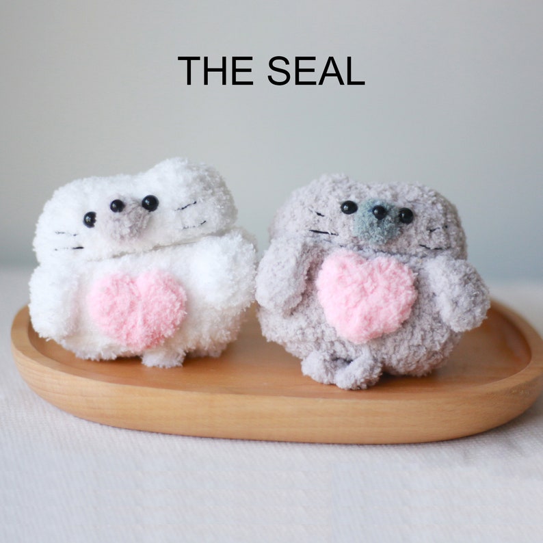 May include: Two plush toy seals, one white and one gray, holding pink hearts. The text "THE SEAL" is above the toys.