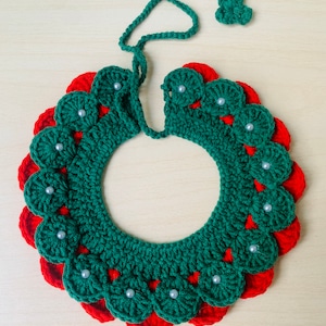 May include: A handmade crochet wreath in a circular shape, featuring a green base with red scalloped edges. The wreath is adorned with small, white pearl-like beads. A green vine with three leaf-shaped accents extends from the top.