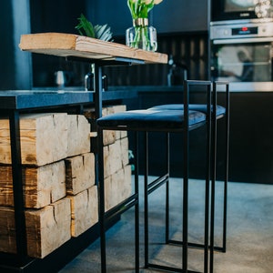 May include: Two black metal bar stools with blue velvet seats. The stools are in front of a kitchen counter with a wooden top and a black base. The counter is made of stacked wooden beams.
