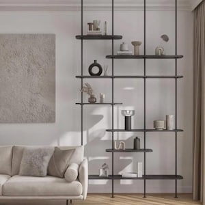 Peut inclure: Une étagère moderne en métal noir avec plusieurs étagères rondes, présentant des vases décoratifs, des livres et de petites sculptures. L'unité est suspendue au plafond, offrant une solution de rangement élégante contre un mur neutre.
