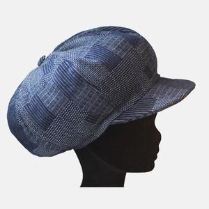 Peut inclure: Un chapeau bleu à motifs avec un petit bord. Le chapeau présente un motif répétitif de petits points et lignes blancs, créant un aspect texturé. Le chapeau est posé sur un fond blanc.