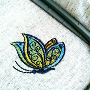 May include: A blue and yellow embroidered butterfly design on a white linen fabric.