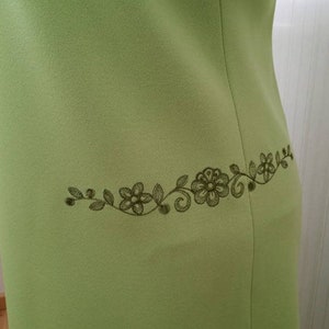 K&ouml;nnte beinhalten: Ein hellgr&uuml;nes Kleid mit einem dunkelgr&uuml;nen, gestickten Blumendesign auf der R&uuml;ckseite.