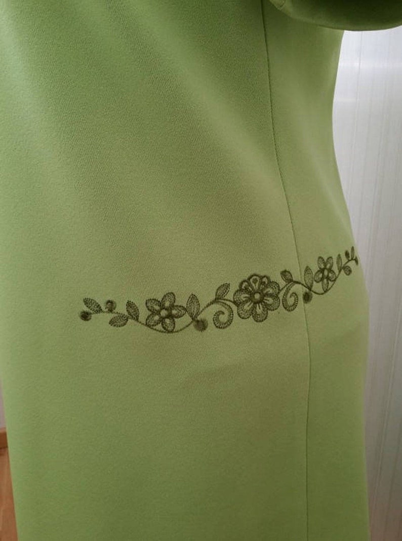 K&ouml;nnte beinhalten: Ein hellgr&uuml;nes Kleid mit einem dunkelgr&uuml;nen, gestickten Blumendesign auf der R&uuml;ckseite.