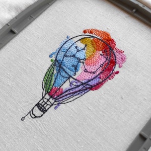 May include: Embroidered design of a hot air balloon with colorful watercolor-like splatter details. The balloon is outlined in black thread and filled with various shades of blue, pink, yellow, and orange.