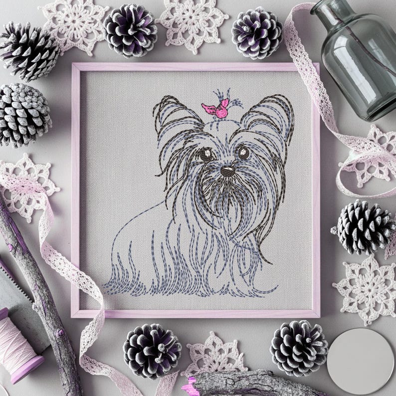 K&ouml;nnte beinhalten: Gerahmte Stickerei eines Yorkshire Terriers mit einem rosa Schmetterling auf dem Kopf. Das Kunstwerk ist von dekorativen Elementen umgeben, darunter Tannenzapfen, Spitzenschneeflocken und eine Glasflasche, alles in Grau-, Wei&szlig;- und Rosat&ouml;nen.
