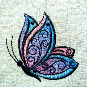May include: Embroidered butterfly design in shades of blue, pink, and black on a beige linen fabric.