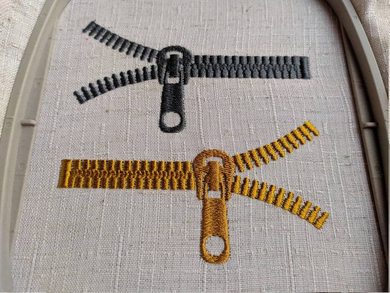 May include: Two embroidered zipper designs on a white fabric. One zipper is black and the other is gold.