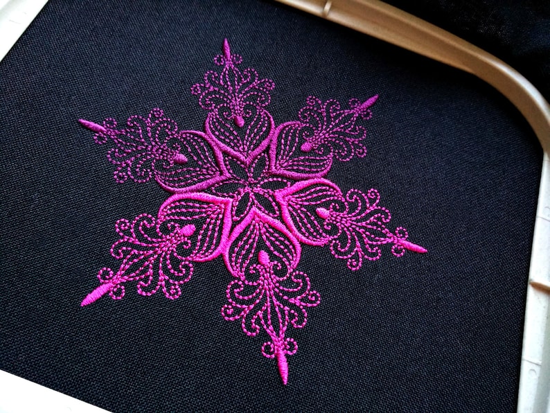 Op de afbeelding: Een roze sneeuwvlok-borduurmotief op een zwarte stoffen achtergrond.