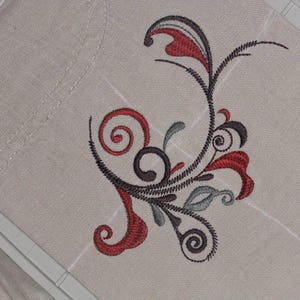 May include: A decorative embroidery design featuring a stylized floral motif with swirling lines and leaves in shades of gray, red, and white.