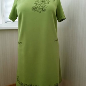 K&ouml;nnte beinhalten: Ein lindgr&uuml;nes Kleid mit kurzen &Auml;rmeln und einem floralen Stickmuster. Die Stickerei befindet sich am Ausschnitt, an den Seiten und am Saum des Kleides.