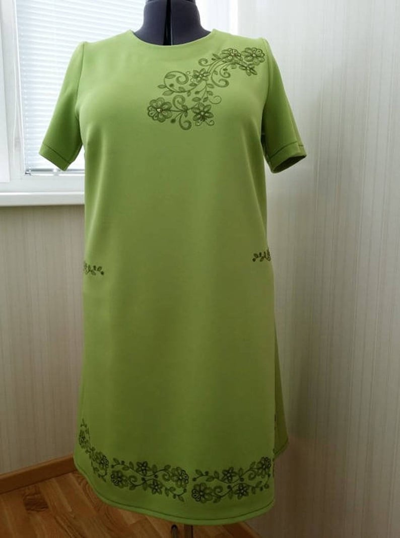 K&ouml;nnte beinhalten: Ein lindgr&uuml;nes Kleid mit kurzen &Auml;rmeln und einem floralen Stickmuster. Die Stickerei befindet sich am Ausschnitt, an den Seiten und am Saum des Kleides.