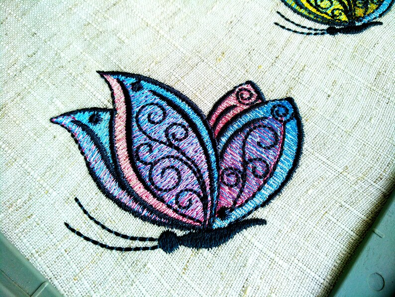 May include: Embroidered butterfly design with blue, pink, and purple colors on a beige fabric background.