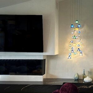a modern living room with a large flat-screen TV mounted on the wall, a fireplace, and a chandelier with colorful glass pieces hanging from the ceiling.