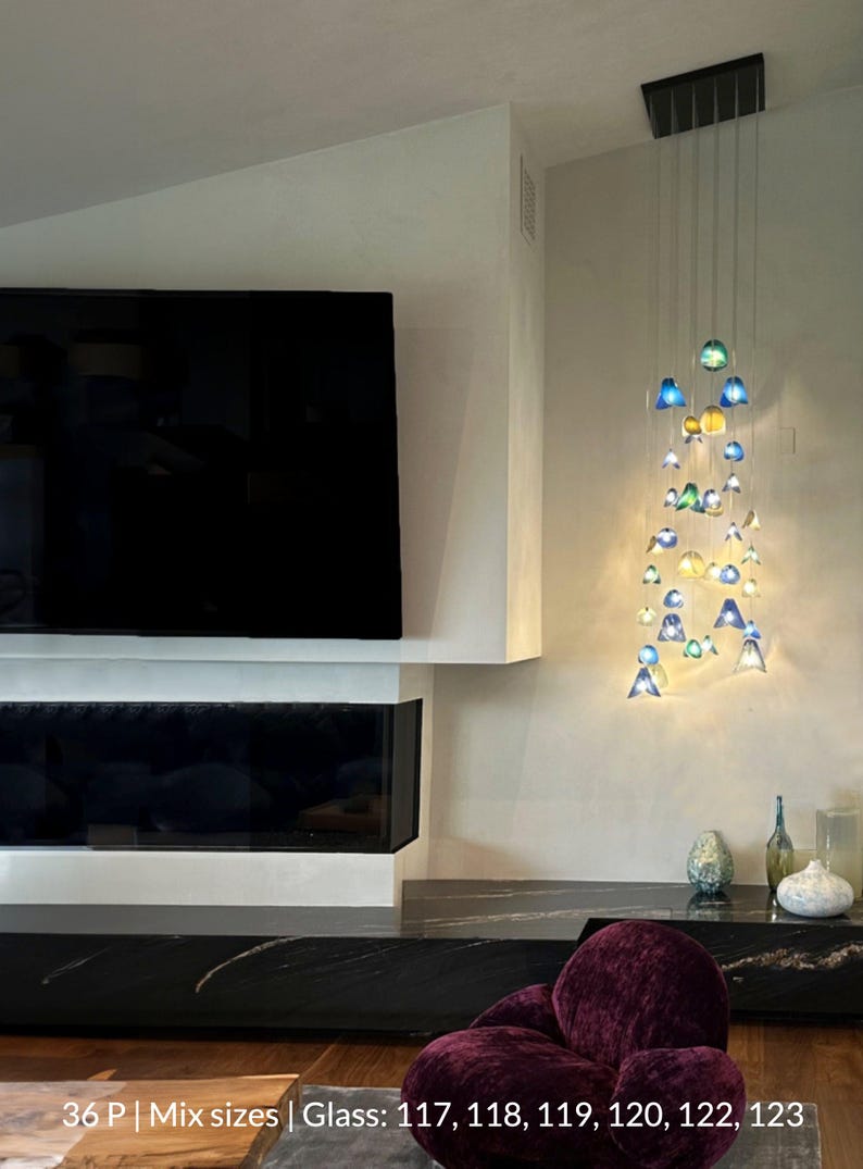 a modern living room with a large flat-screen TV mounted on the wall, a fireplace, and a chandelier with colorful glass pieces hanging from the ceiling.