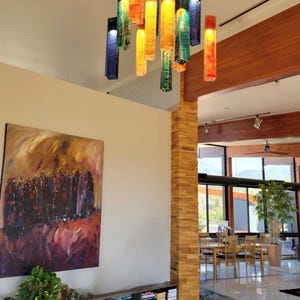 a modern interior with a large painting on the wall, a bookshelf filled with books, and a set of hanging pendant lights.