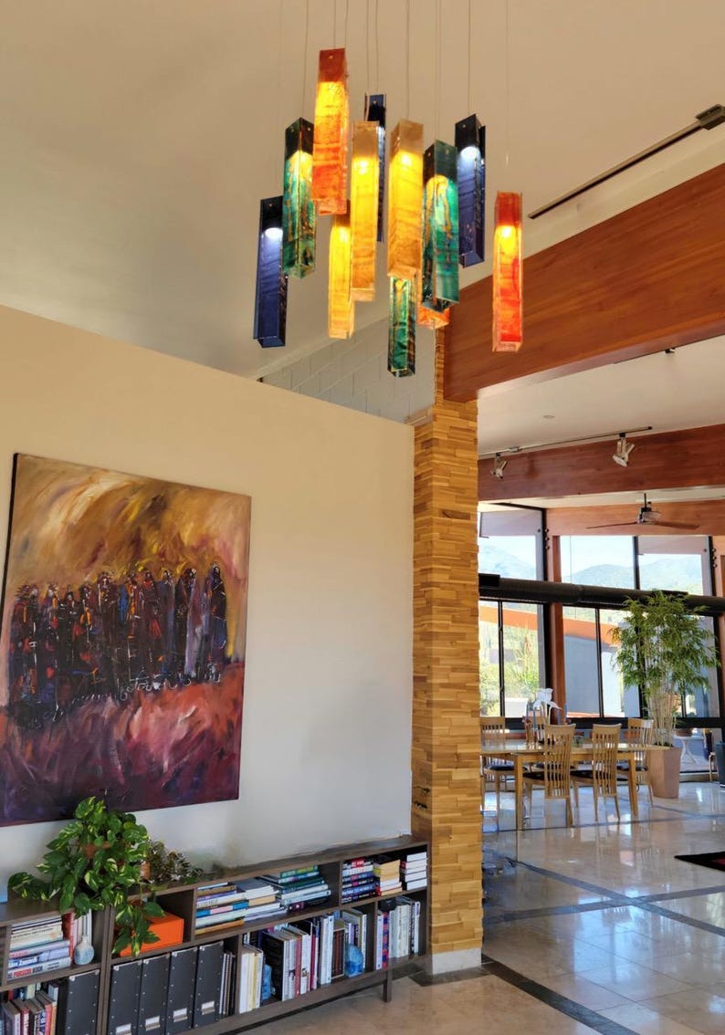 a modern interior with a large painting on the wall, a bookshelf filled with books, and a set of hanging pendant lights.