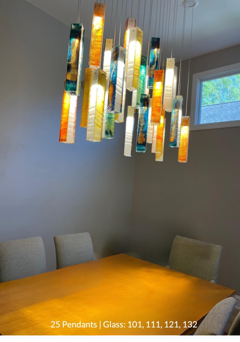 a modern dining room with a wooden table and six chairs. The table is illuminated by a hanging chandelier composed of colorful glass rods that cast a warm glow throughout the room.
