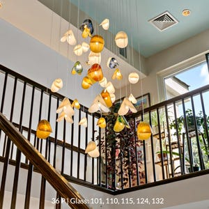 a staircase with a unique and artistic lighting display hanging from the ceiling. The display consists of numerous glass spheres suspended from the ceiling, each with a different color and shape, creating a visually striking and creative atmosphere.