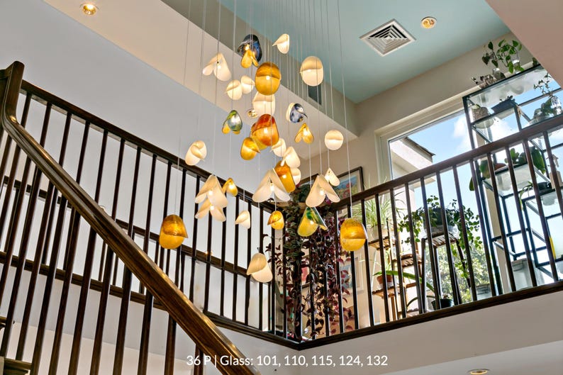 a staircase with a unique and artistic lighting display hanging from the ceiling. The display consists of numerous glass spheres suspended from the ceiling, each with a different color and shape, creating a visually striking and creative atmosphere.