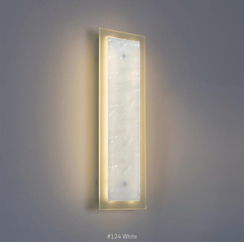 May include: A rectangular wall sconce with a frosted white center panel and a soft yellow frame. The sconce is mounted on a gray wall and has the text "#124 White" at the bottom.