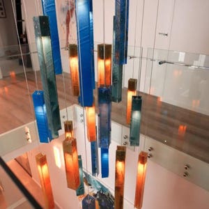 a modern and stylish interior design with a striking chandelier made of colorful glass rods suspended from the ceiling. The chandelier has a mix of blue, orange, and green glass rods, creating a visually appealing and vibrant display. The overall design and arrangement of the chandelier contribute to the contemporary and sophisticated atmosphere of the space.