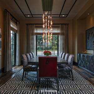 a luxurious dining room with a large wooden table surrounded by gray chairs, a red chair, and a chandelier with multiple lights hanging above the table. The room features a large window with curtains, and there are paintings on the walls. The overall design and decor create an elegant and sophisticated atmosphere.