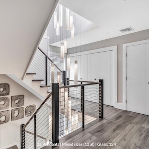 a modern and stylish interior design with a staircase, a black railing, and a large chandelier hanging from the ceiling. The staircase has a mix of different sizes and styles of pendant lights, creating a visually appealing and contemporary look. The overall design appears to be a combination of modern and traditional elements, with a focus on clean lines and minimalist aesthetics.