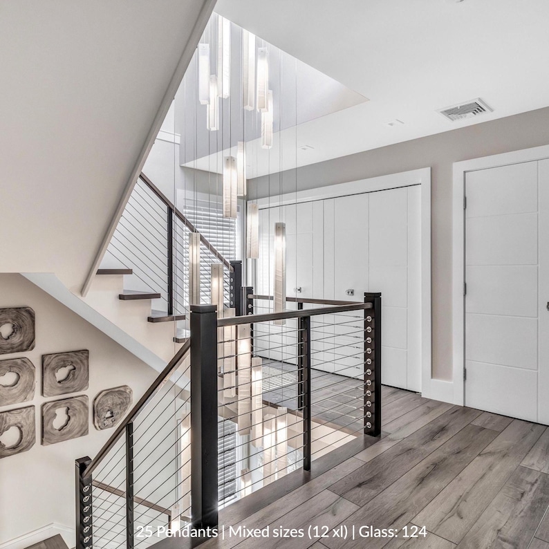 a modern and stylish interior design with a staircase, a black railing, and a large chandelier hanging from the ceiling. The staircase has a mix of different sizes and styles of pendant lights, creating a visually appealing and contemporary look. The overall design appears to be a combination of modern and traditional elements, with a focus on clean lines and minimalist aesthetics.